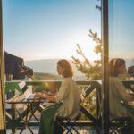Frau sitzt mit Laptop auf einem Balkon bei Sonnenuntergang – symbolisch für die Flexibilität als Escort in Frankfurt